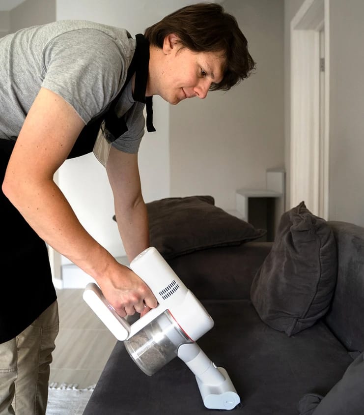 Vacuuming a Sofa Man using a handheld cordless vacuum to clean a gray couch.