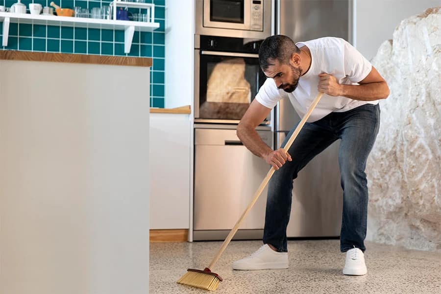 Sweeping the Kitchen Floor Man in a white shirt sweeping a kitchen floor with a broom.